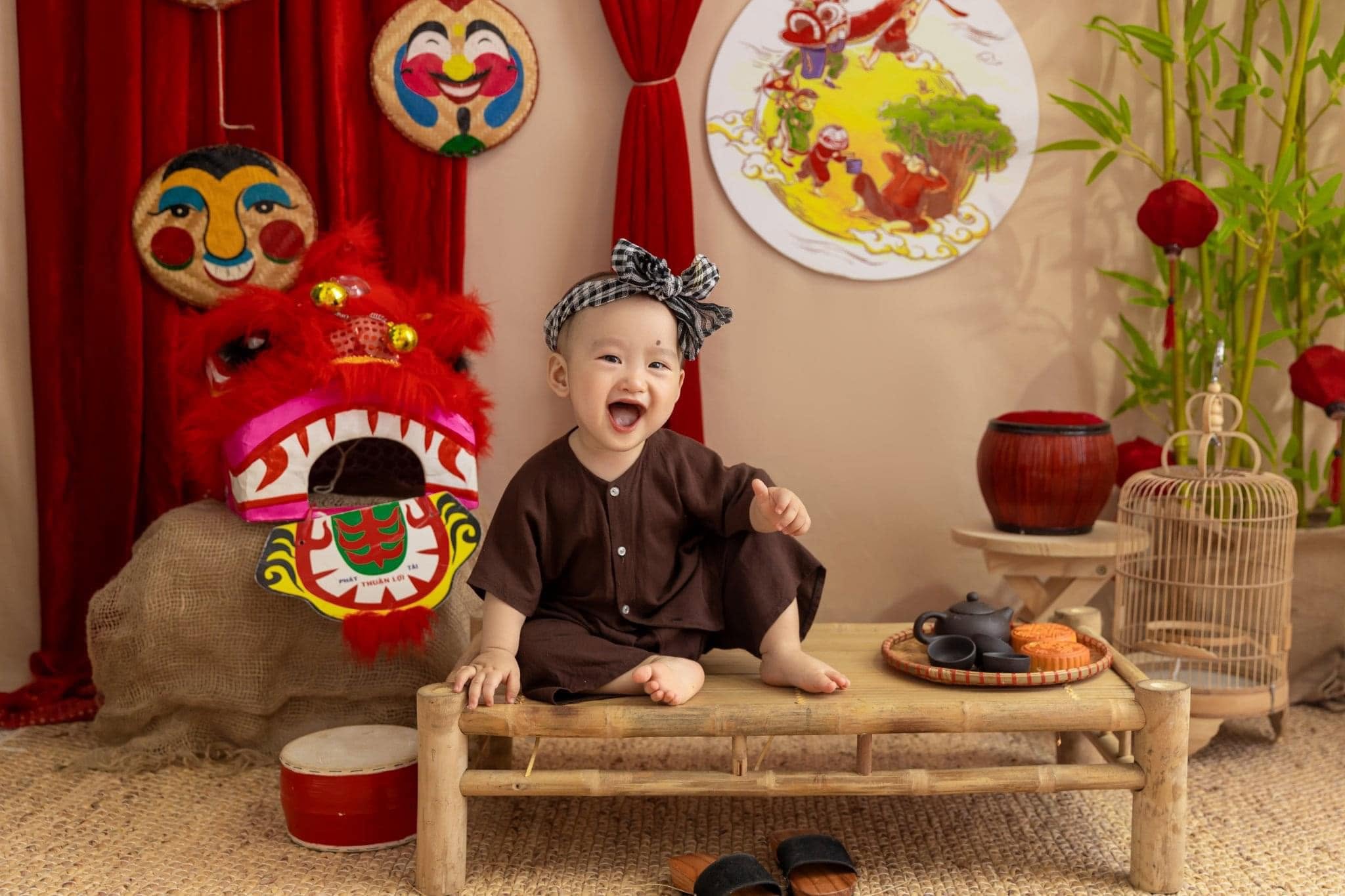 Em bé áo bà ba nâu cười lớn bên đầu lân đỏ tại bối cảnh Trung thu Kam Studio